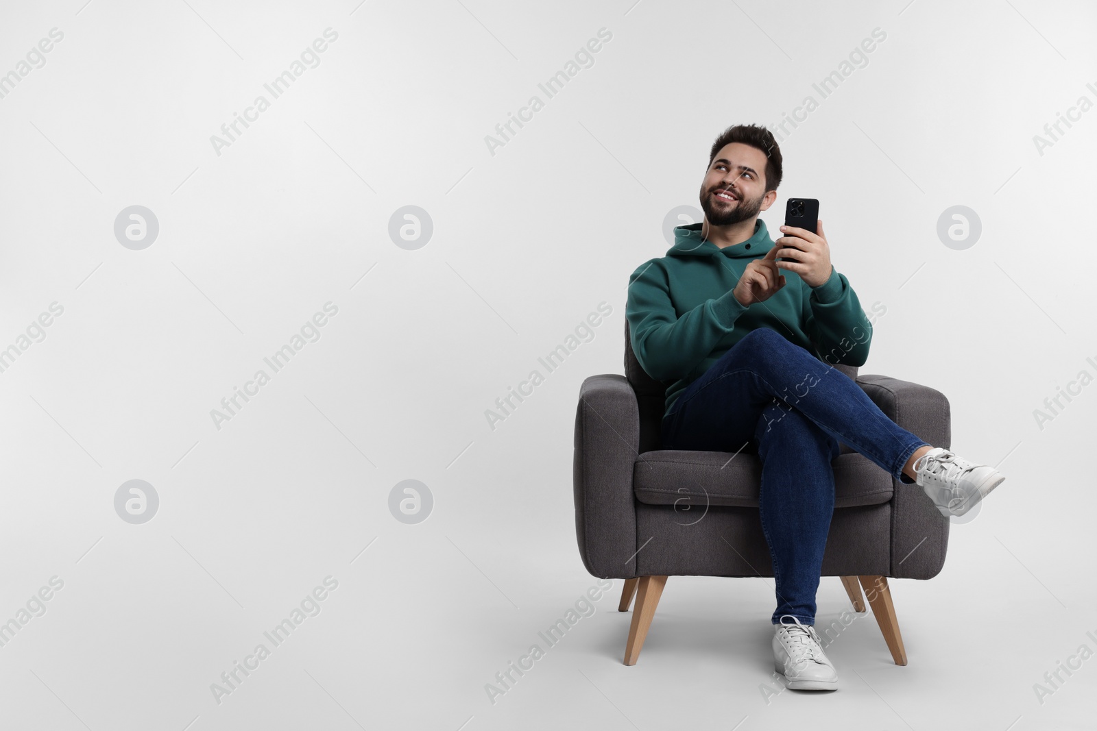 Photo of Happy young man using smartphone in armchair on white background, space for text