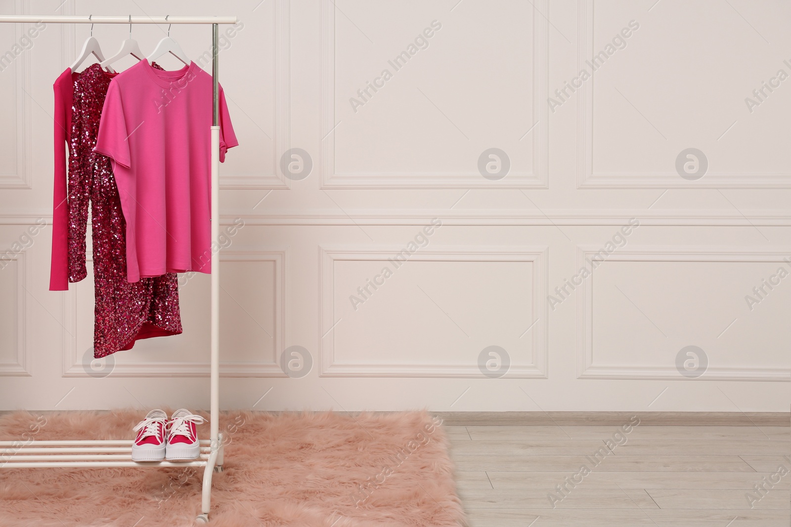 Photo of Rack with different stylish women`s clothes and sneakers near white wall in showroom, space for text