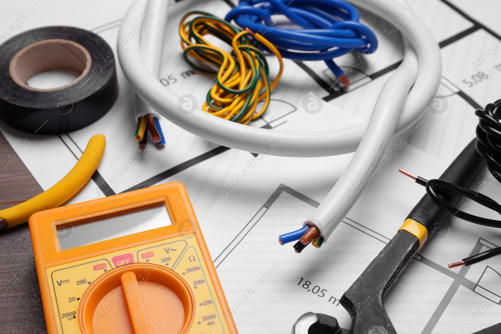 Photo of Different wires, tools and electrical schemes on wooden table, closeup