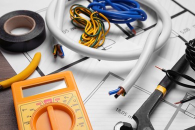 Photo of Different wires, tools and electrical schemes on wooden table, closeup