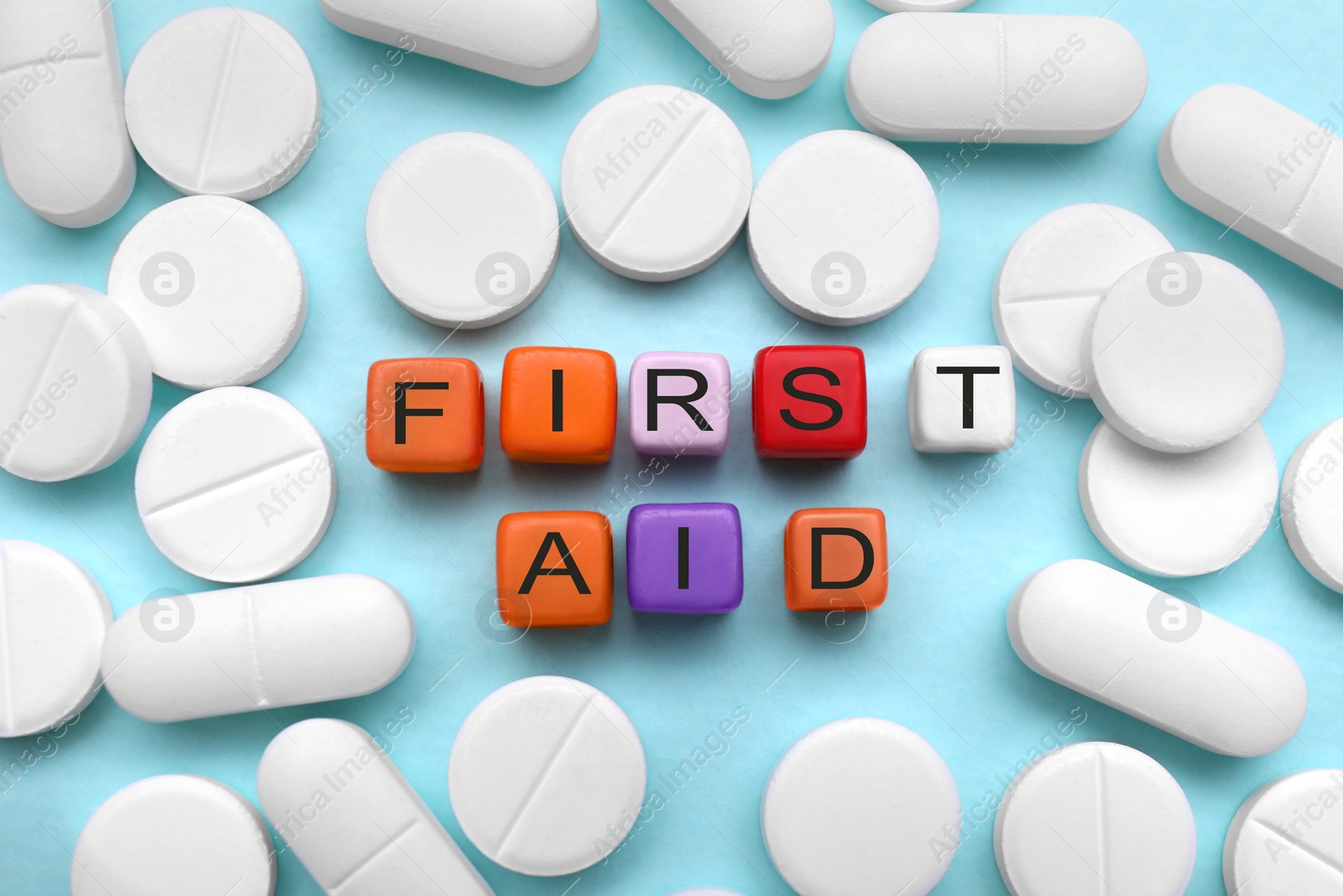 Photo of Colorful cubes with words First Aid and pills on light blue background, flat lay