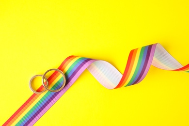 Photo of Wedding rings and rainbow ribbon on color background, top view. Gay symbol