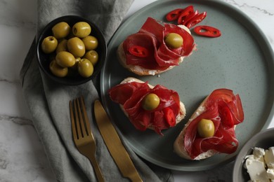 Photo of Delicious sandwiches with bresaola, cream cheese and olives served on white marble table, flat lay