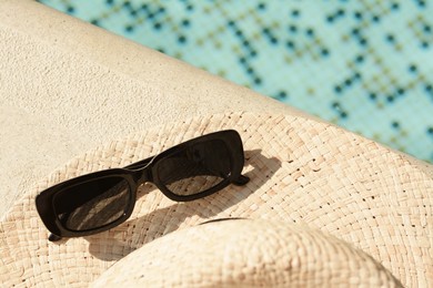 Photo of Stylish hat and sunglasses near outdoor swimming pool on sunny day. Space for text