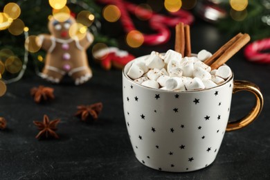 Photo of Delicious hot chocolate with marshmallows and cinnamon near Christmas decor on black table, closeup. Space for text