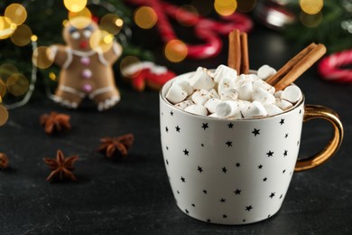 Delicious hot chocolate with marshmallows and cinnamon near Christmas decor on black table, closeup. Space for text