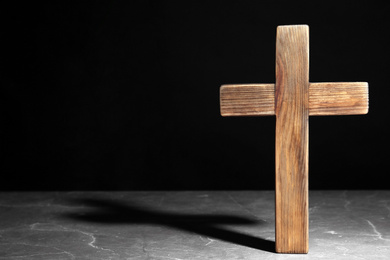 Wooden Christian cross on brown marble table against black background, space for text. Religion concept