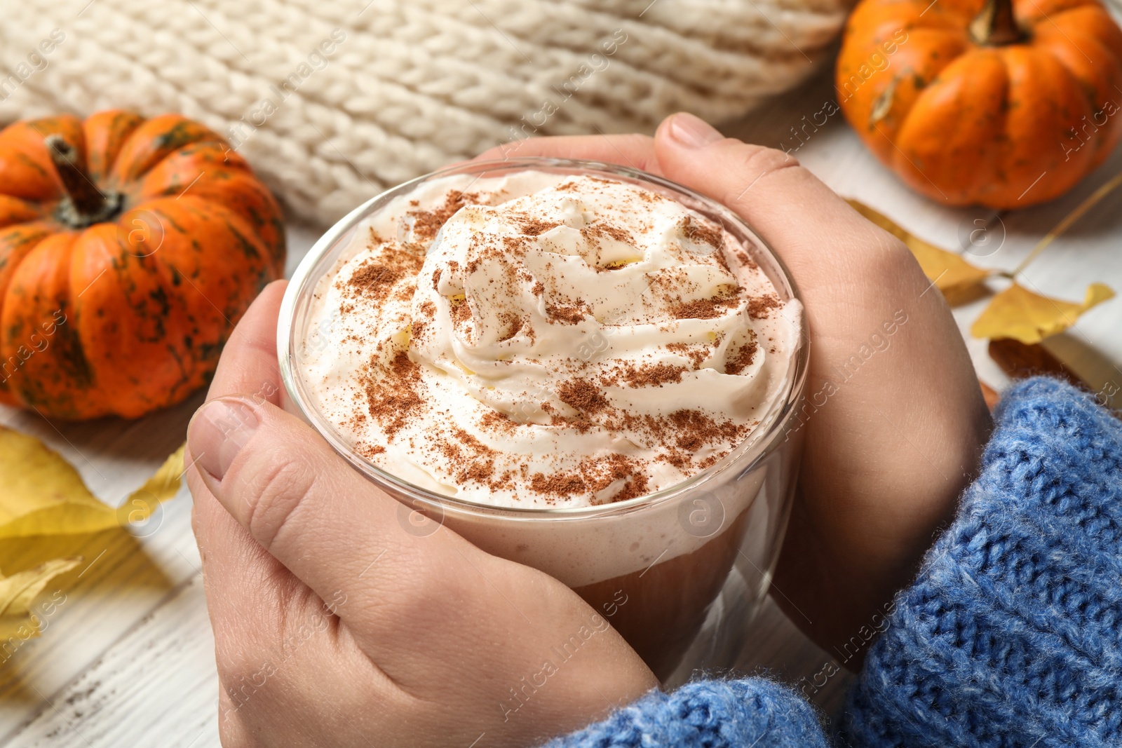 Photo of Woman holding tasty pumpkin latte at white table, closeup