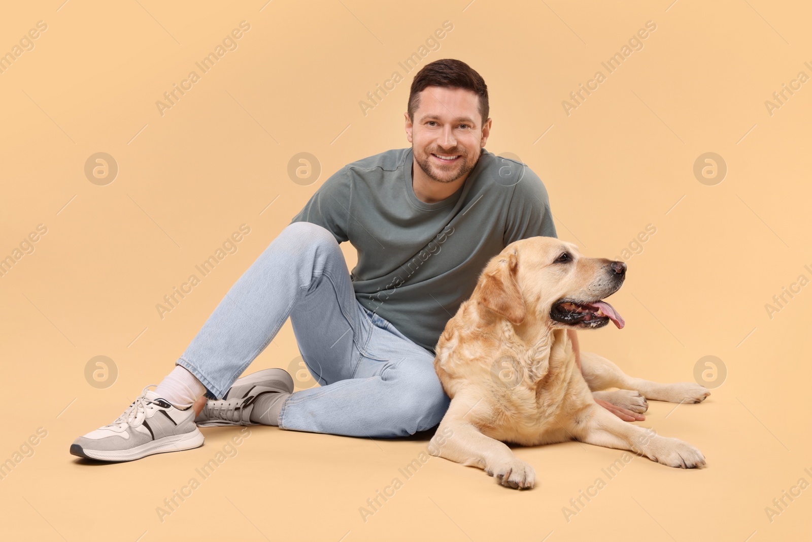 Photo of Man with adorable Labrador Retriever dog on beige background. Lovely pet