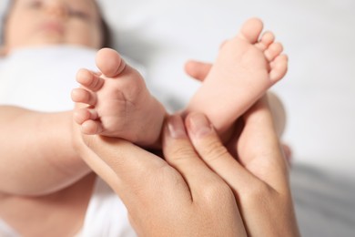 Photo of Mother holding legs of her little baby on bed, closeup