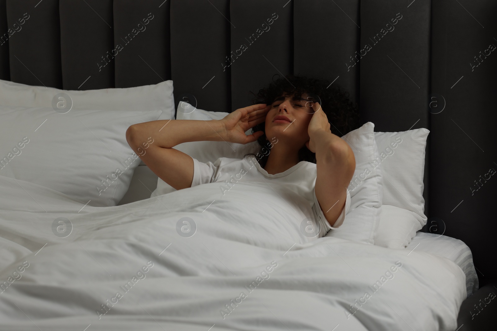 Photo of Young woman suffering from headache in bed at night