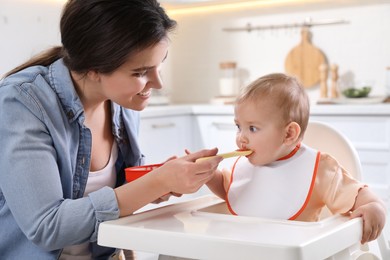 Photo of Mother feeding her cute little baby in kitchen