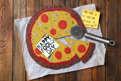 Photo of Cardboard pizza and Happy Fools' Day note on wooden table, flat lay