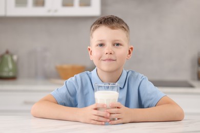Photo of Cute boy with glass of milk at white table in kitchen