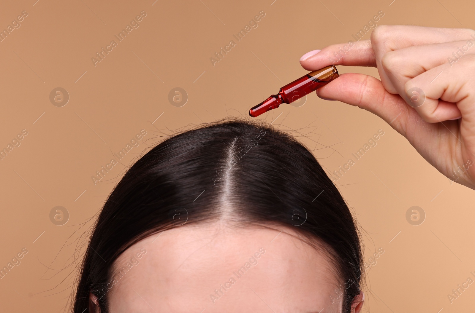 Photo of Beautiful young woman using ampoule for hair treatment on beige background, closeup