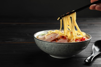 Photo of Woman eating delicious ramen with chopsticks at black wooden table, closeup and space for text. Noodle soup