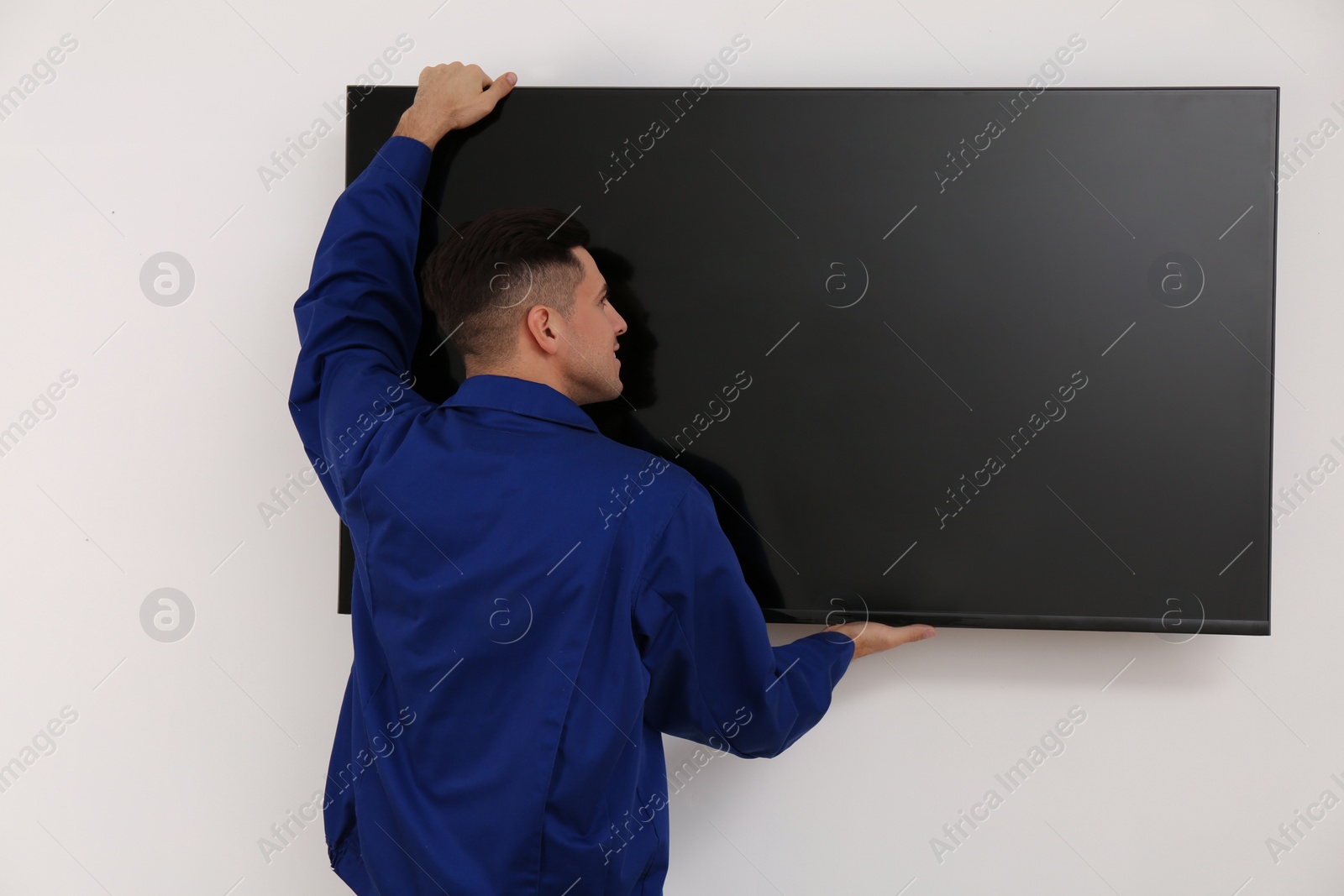 Photo of Professional technician installing modern flat screen TV on wall indoors