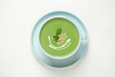 Photo of Cup of healthy green soup with fresh spinach on white wooden table, top view