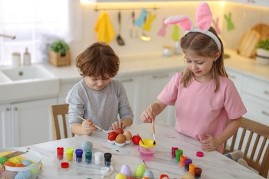 Easter celebration. Cute children with bunny ears painting eggs at white marble table in kitchen