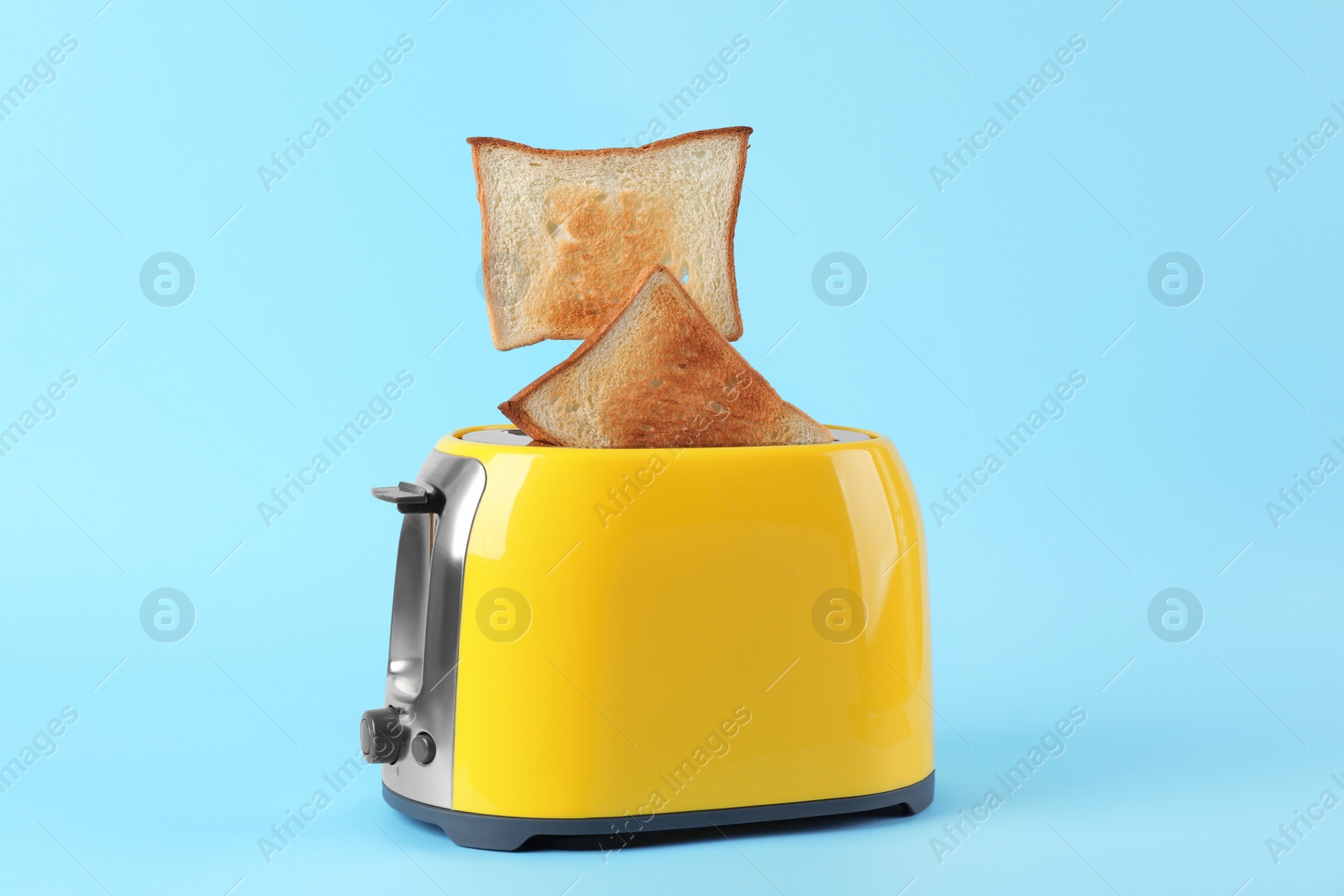 Photo of Bread slices popping up from modern toaster on light blue background