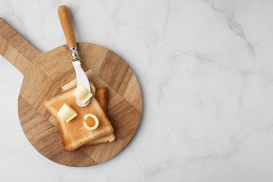 Photo of Tasty butter curls, knife and toasts on white marble table, top view. Space for text