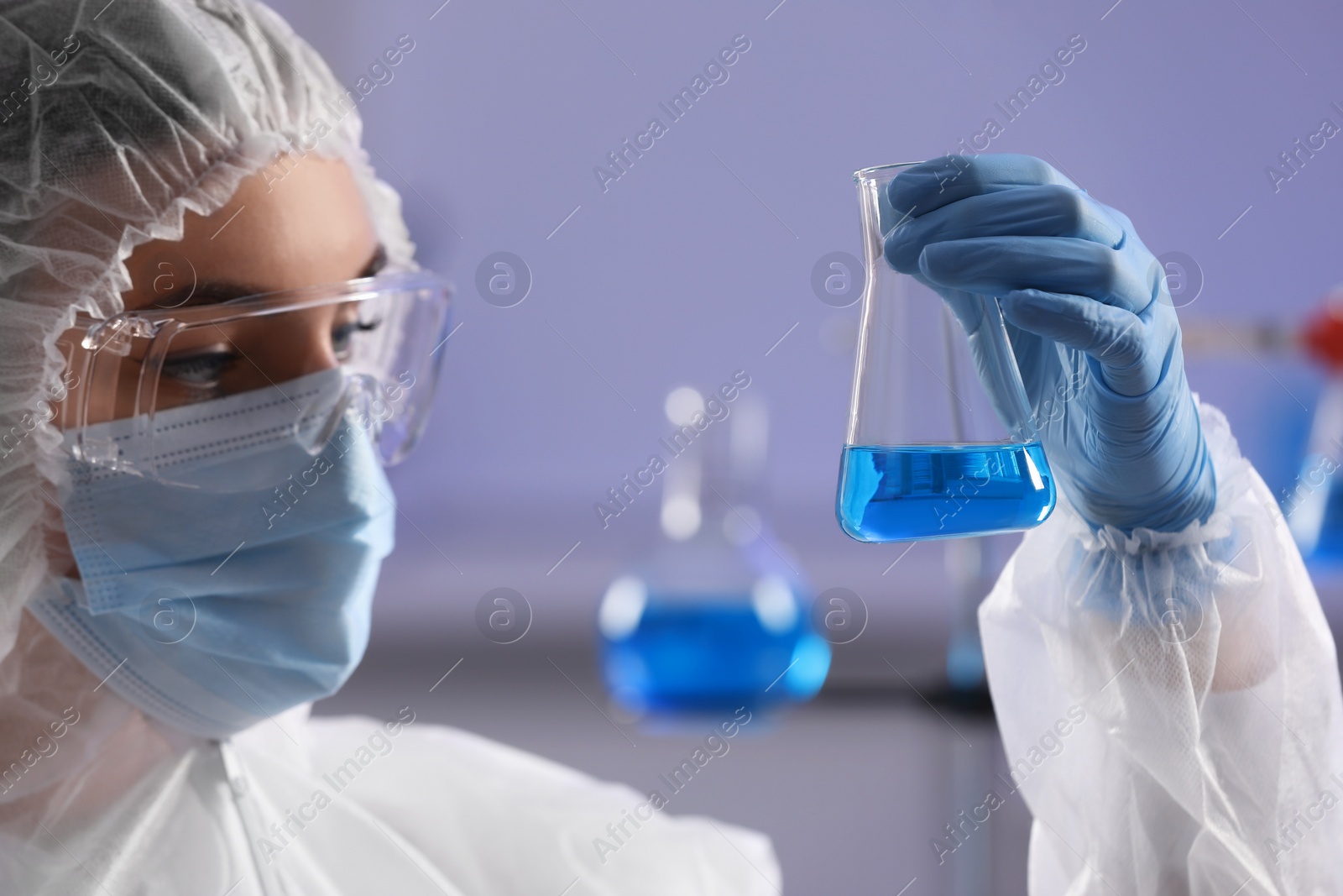 Photo of Scientist holding flask with light blue liquid in laboratory, closeup