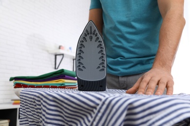 Photo of Man ironing shirt on board at home, closeup