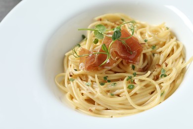 Photo of Tasty spaghetti with prosciutto and microgreens on plate, closeup. Exquisite presentation of pasta dish