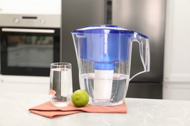 Photo of Water filter jug, glass and lime on light marble table in kitchen, closeup