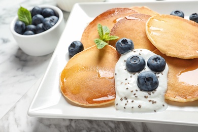 Plate of tasty pancakes with blueberries, sauce and mint on marble table, closeup
