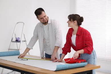 Photo of Woman and man applying glue onto wallpaper sheet at wooden table indoors