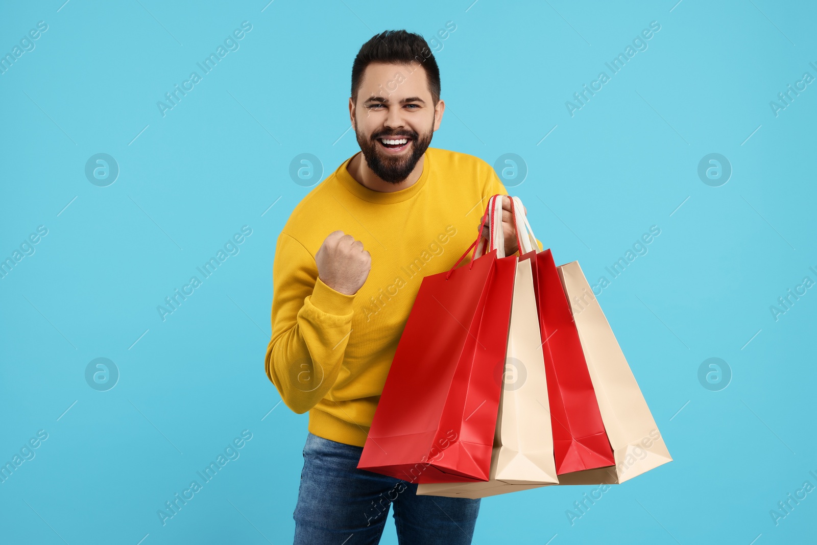 Photo of Excited man with many paper shopping bags on light blue background