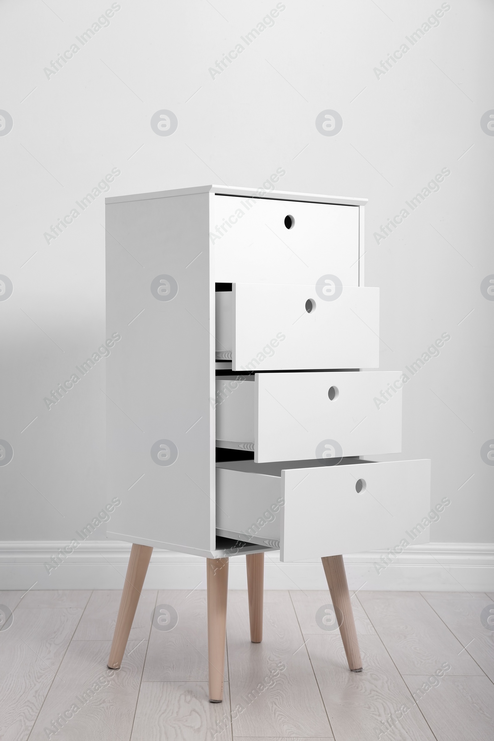 Photo of Stylish chest of drawers near white wall. Furniture for wardrobe room