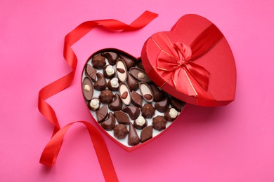 Photo of Heart shaped box with delicious chocolate candies and ribbon on pink background, flat lay