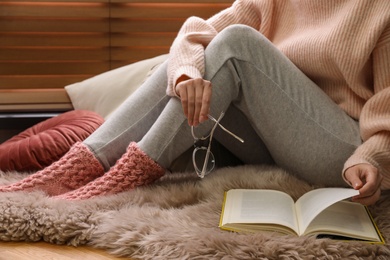 Photo of Woman in knitted socks reading book on floor at home, closeup