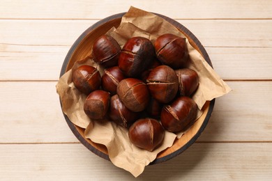 Roasted edible sweet chestnuts in bowl on wooden table, top view