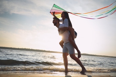 Photo of Happy couple playing with kite on beach near sea at sunset. Spending time in nature