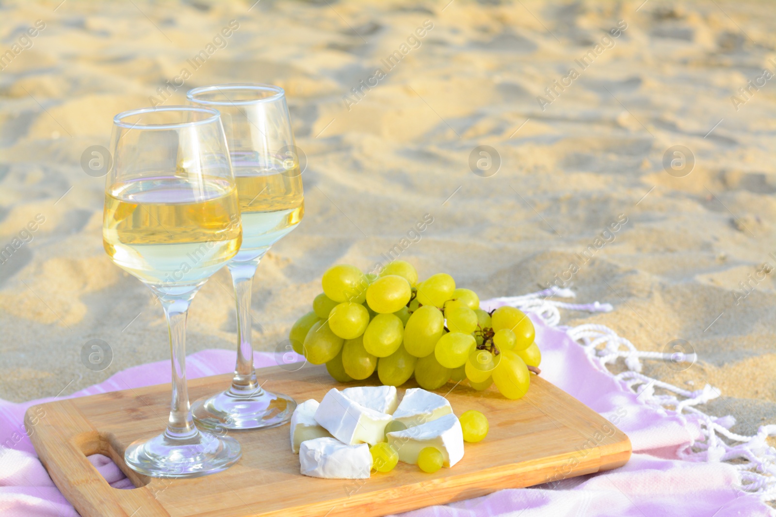 Photo of Glasses with white wine and snacks on beach sand outdoors. Space for text