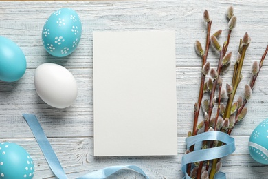 Flat lay composition with painted Easter eggs and blank card on wooden background, space for text