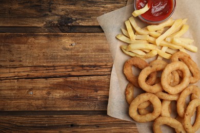 Photo of Delicious onion rings, fries and ketchup on wooden table, top view. Space for text