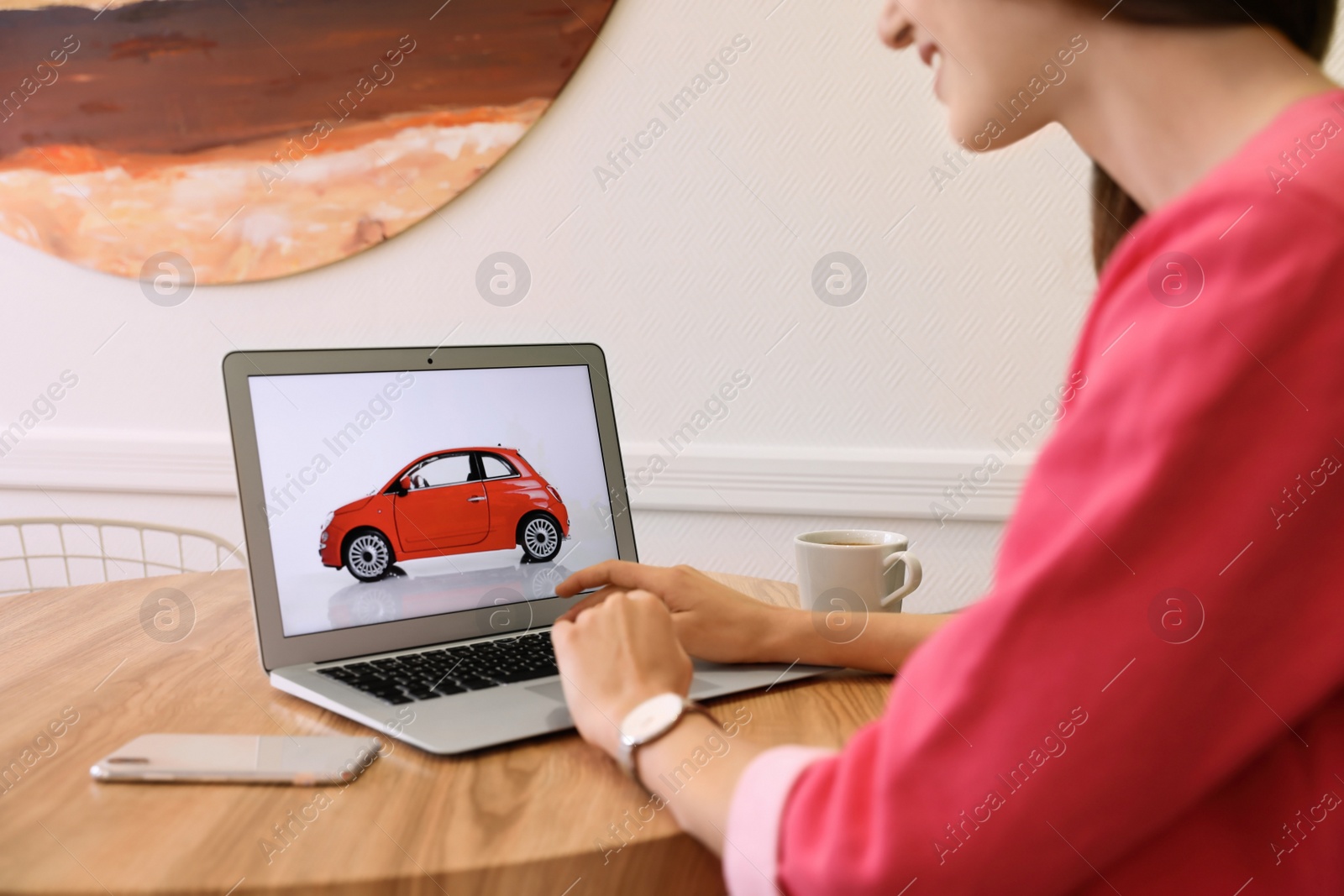 Photo of Woman using laptop to buy car at wooden table indoors, closeup