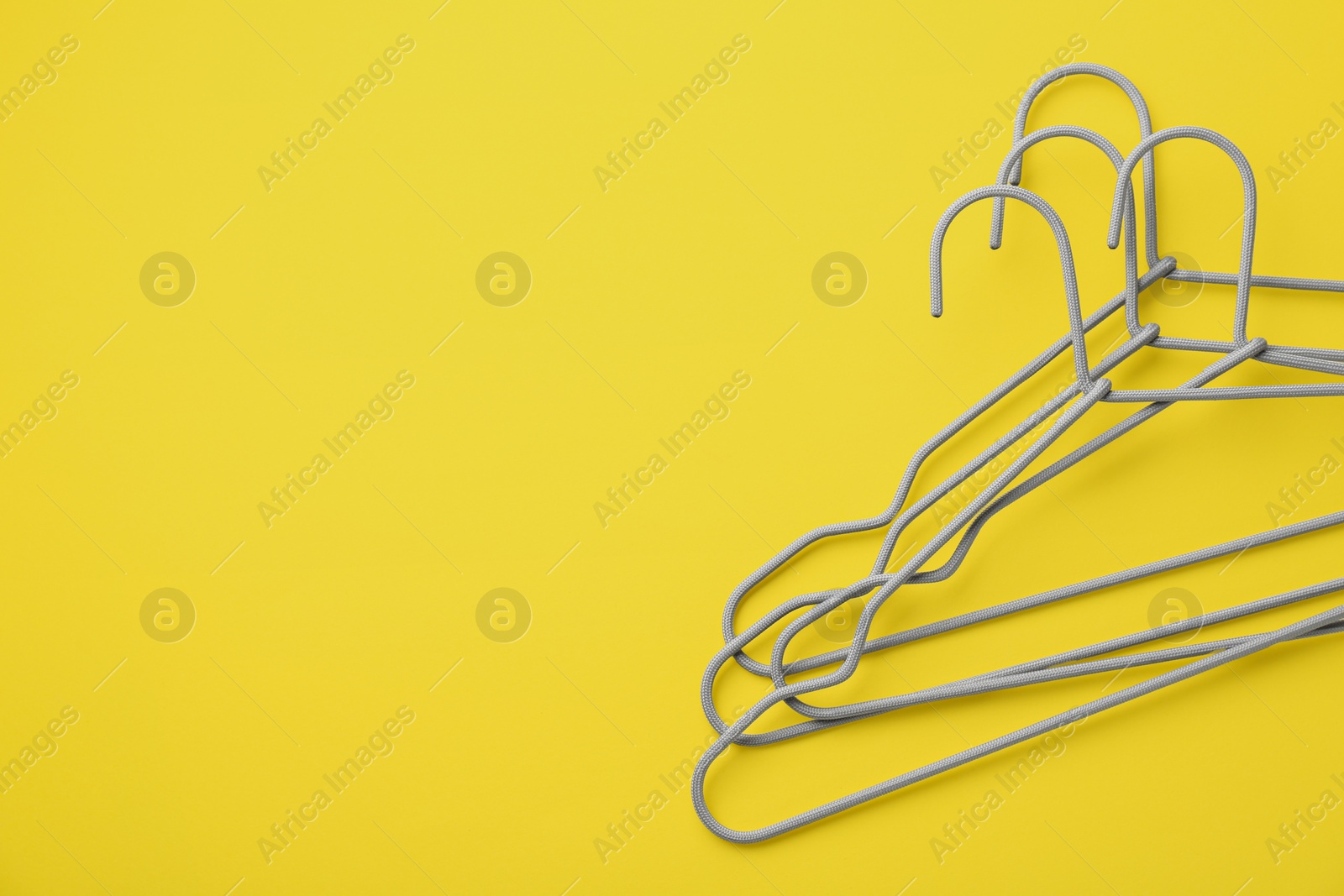 Photo of Hangers on yellow background, top view. Space for text