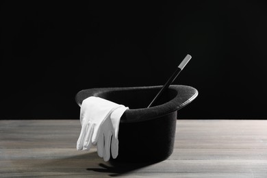 Photo of Magician's hat, gloves and wand on white wooden table against black background