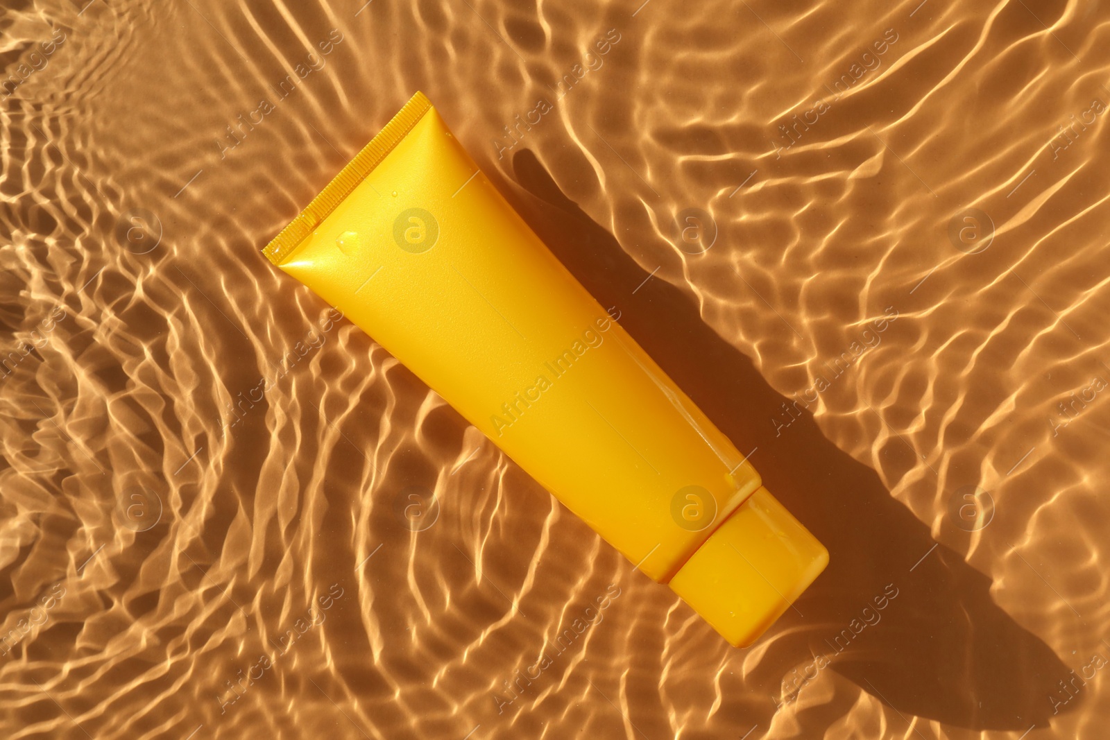 Photo of Tube with moisturizing cream in water on orange background, top view