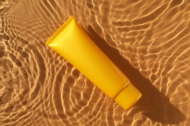 Tube with moisturizing cream in water on orange background, top view