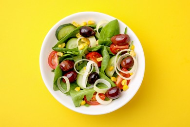 Photo of Bowl of tasty salad with leek and olives on yellow table, top view