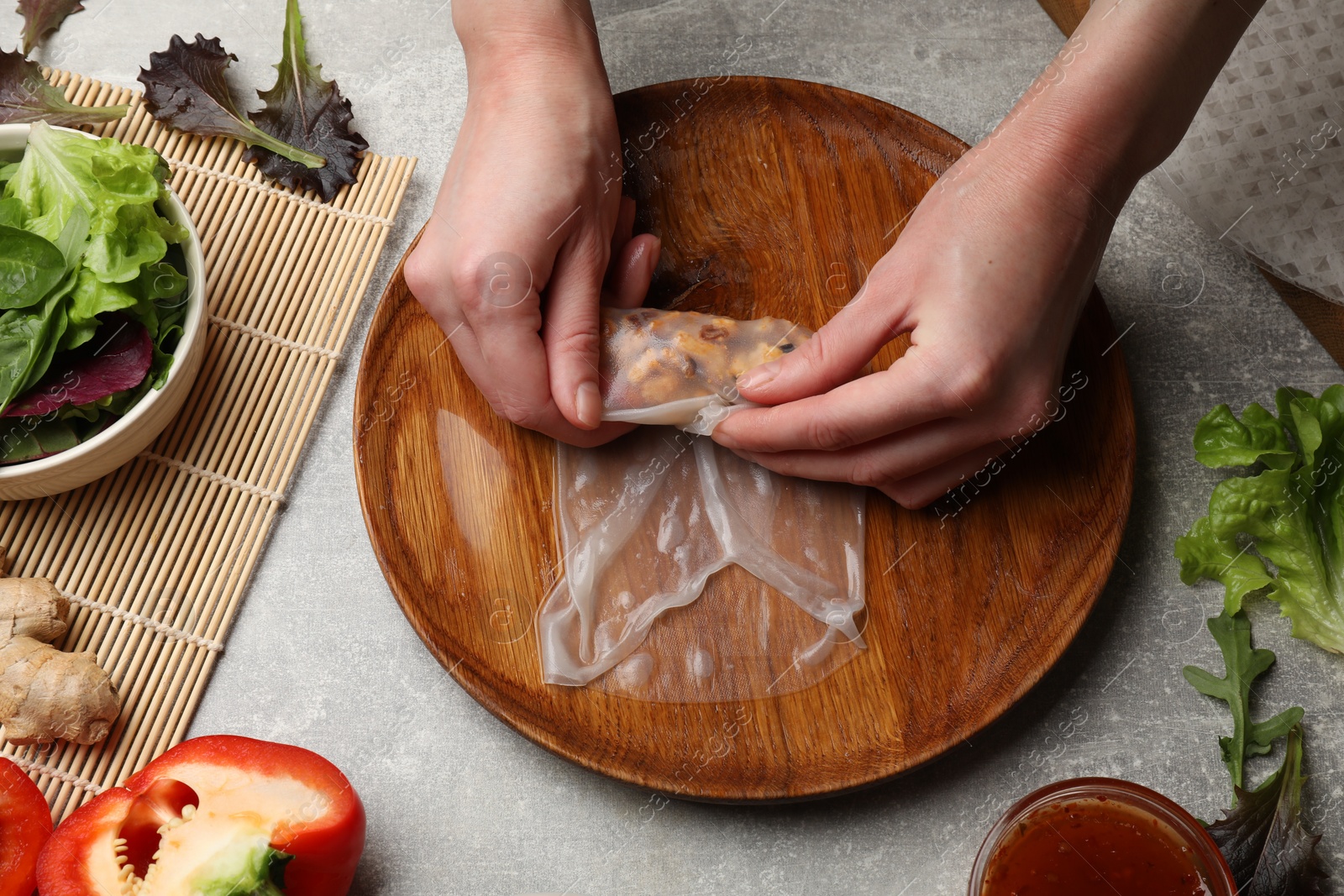 Photo of Woman making tasty spring roll at grey table, top view