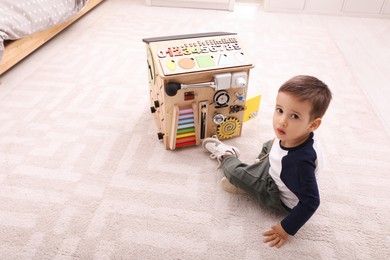 Photo of Little boy playing with busy board on floor at home
