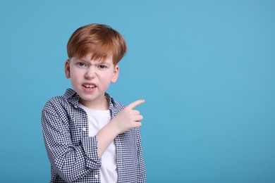 Photo of Surprised little boy pointing at something on light blue background, space for text