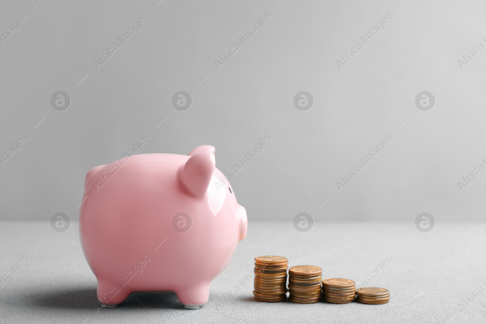 Photo of Piggy bank and coins on table against grey background. Space for text